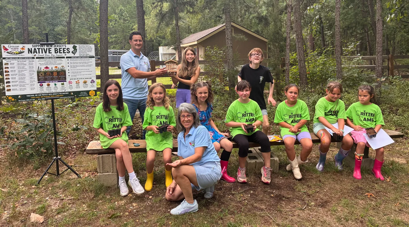 The Critter Camp group with Don Grasso and an Alliance volunteer in front of the Support New Jersey's Native Bees banner, kids holding their seedling trays