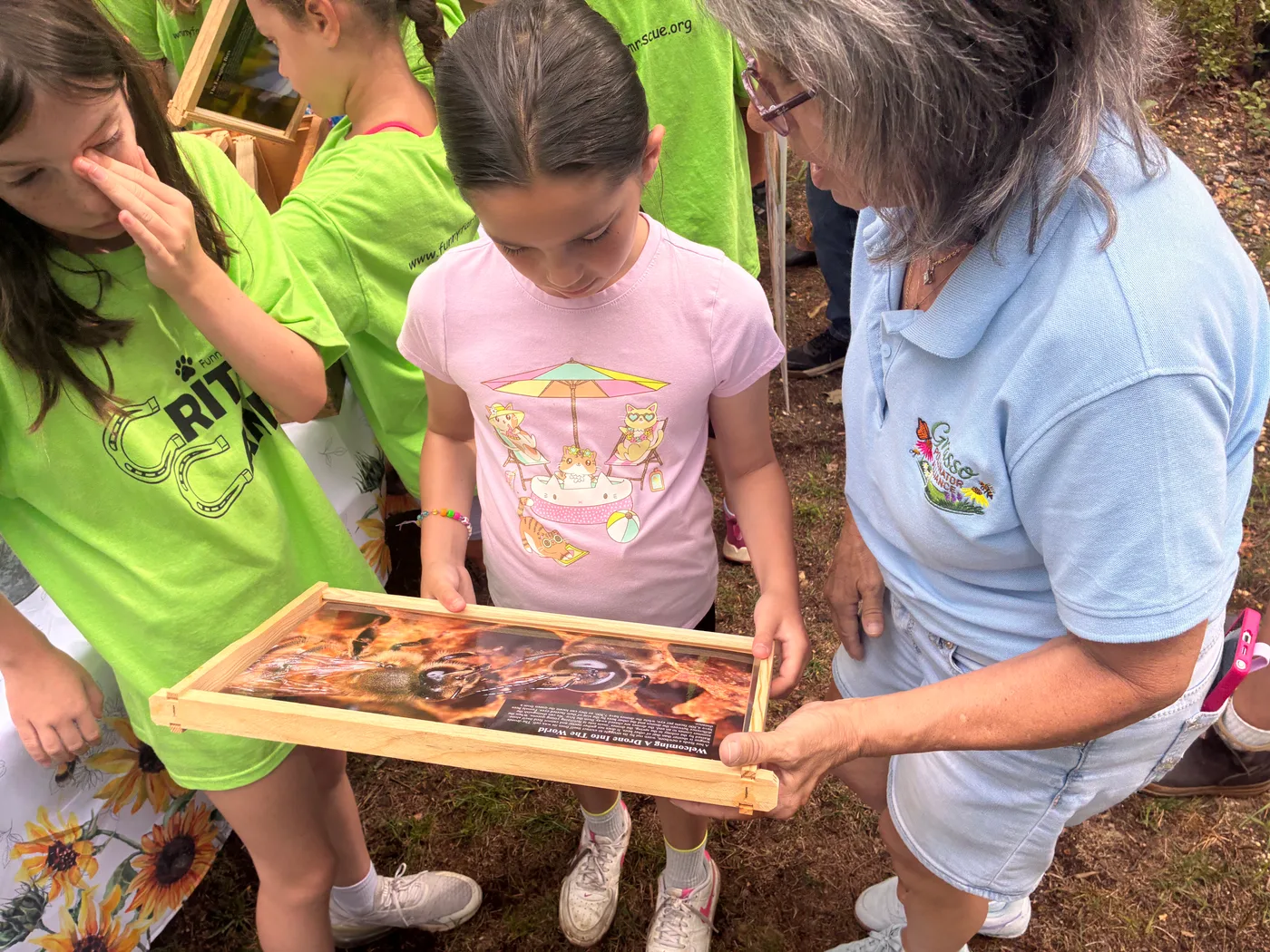 A girl studying a framed educational display about drones held by a Grasso Pollinator Alliance volunteer