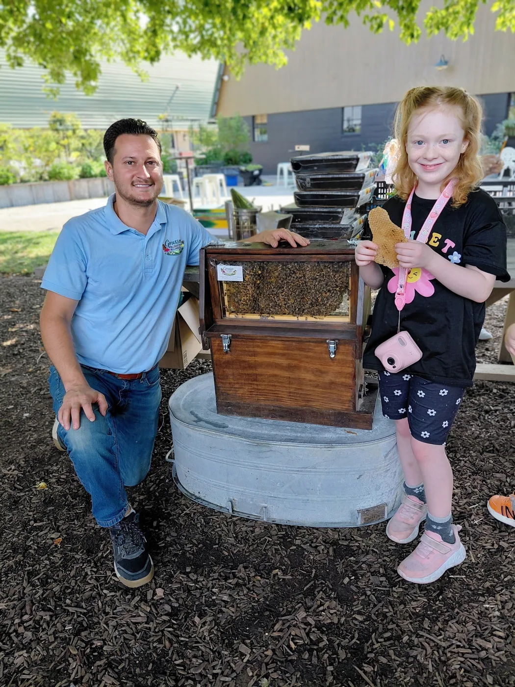 A young visitor standing with founder Don Grasso beside a live observation hive