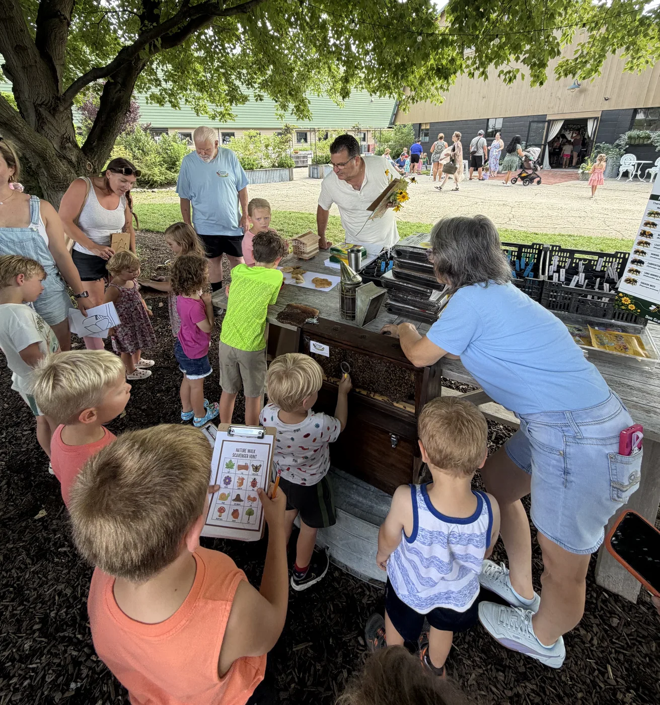 Children gathered around a table of hive frames while a beekeeper explains them