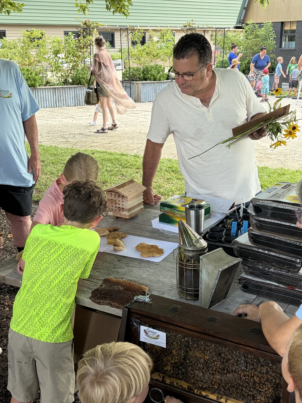 A beekeeper lifting a honeycomb frame so children can see the comb up close
