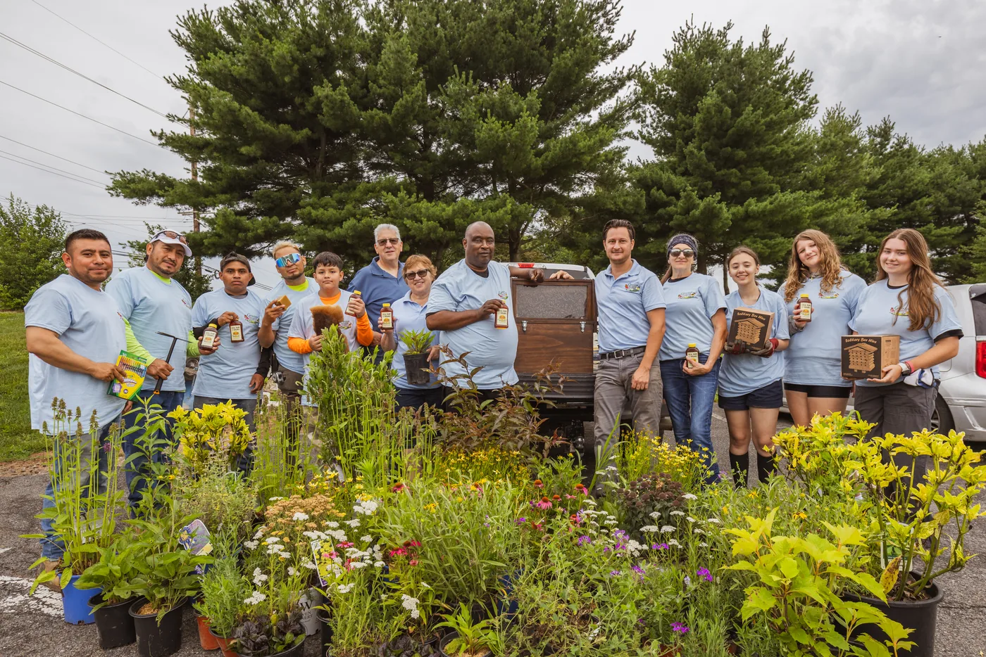 Grasso Pollinator Alliance volunteers in blue shirts gathered with native plants and an observation hive at the Kingsway pollinator garden install