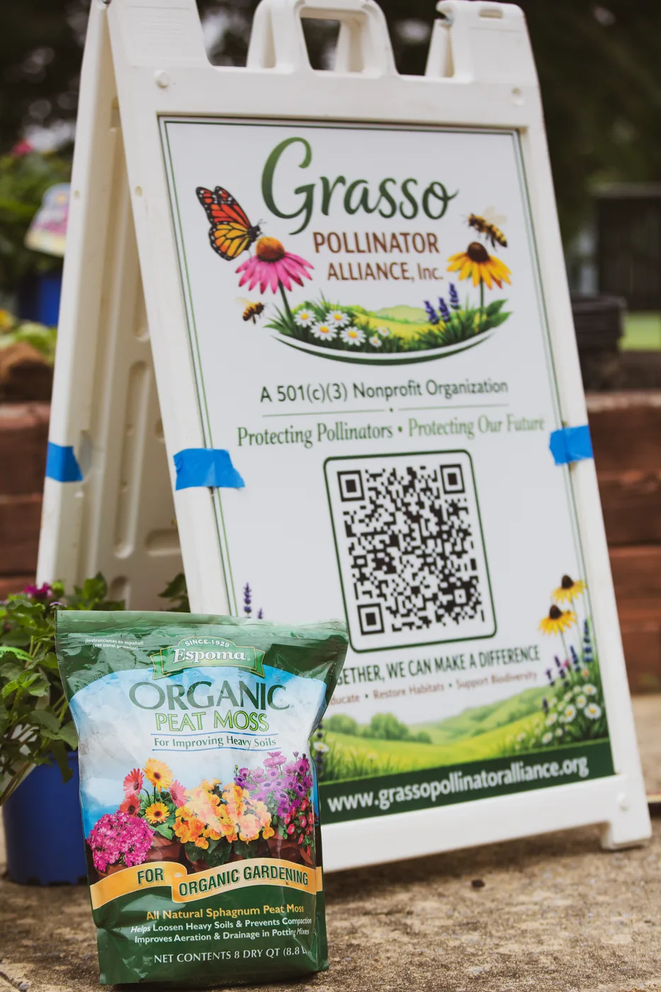 A bag of organic peat moss leaning against the Grasso Pollinator Alliance sign
